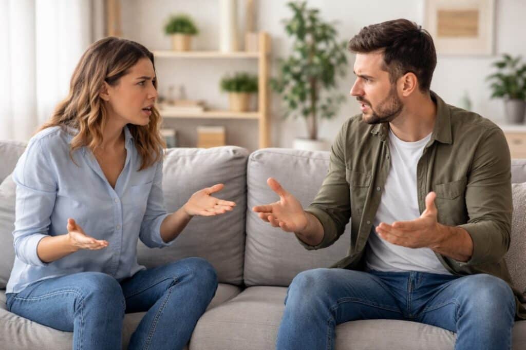 Adult siblings arguing on sofa during intense family conflict, representing brother and sister relationship tension
